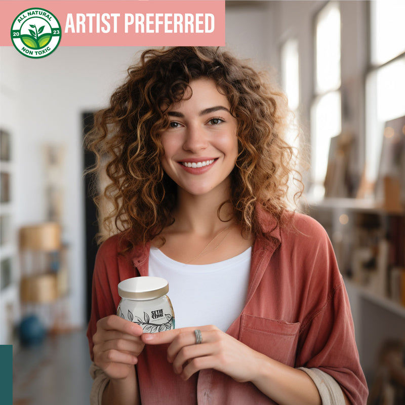 a happy, smiling woman with curly brown hair and coral pink shirt holding a jar of wax polish